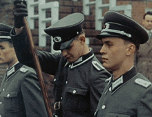 three men in military uniforms are standing in front of a brick building
