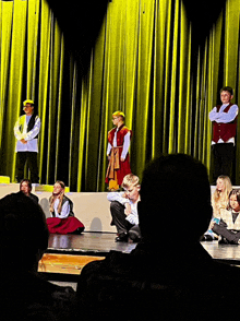 a group of children are on a stage with yellow curtains