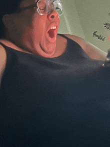a woman wearing glasses and a black tank top is yawning with her mouth open