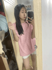 a girl in a pink shirt is taking a selfie in a mirror