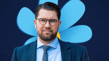 a man wearing glasses and a blue suit is standing in front of a blue flower