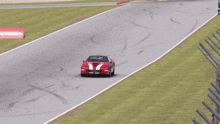a red car with white stripes on the side is driving down a track