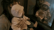 a woman is holding a baby in her arms and the baby is looking at the reflection of the woman in the mirror .