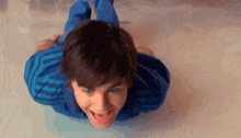 a young man in a blue striped shirt is laying on his stomach on the floor