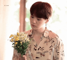 a young man in a floral shirt is holding a bouquet of yellow flowers .