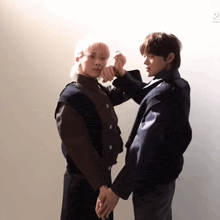 two young men are holding hands while standing next to each other against a white wall