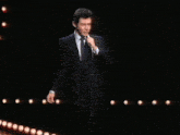 a man in a suit is standing on a stage holding a microphone in front of a crowd