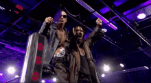 a couple of men standing next to each other with their arms in the air and one of them has a skull on his arm