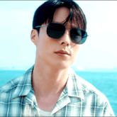 a man wearing sunglasses and a plaid shirt is standing in front of the ocean