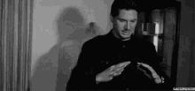 a man in a black shirt is standing in front of a wall and looking at his phone .