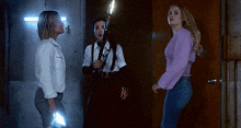 a woman in a purple sweater is standing next to two other women in a dark room
