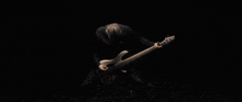 a man in a black shirt is playing a bass guitar in the dark
