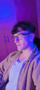 a man wearing glasses and a white shirt is sitting in front of a purple light