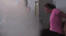 a woman in a pink shirt is standing in front of a smokey wall