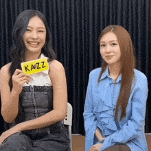 two women are sitting next to each other and one of them is holding a sign that says kazz .