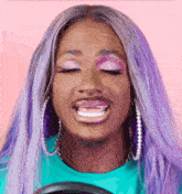 a woman with purple hair and pink eye shadow is smiling with her eyes closed