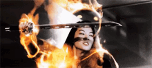 a woman is holding a sword with flames behind her