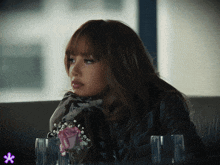 a woman sits at a table with two glasses and a vase of baby 's breath