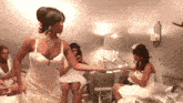 a woman in a wedding dress is dancing in a room with other women .