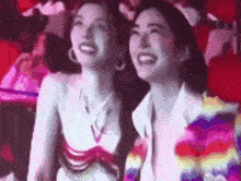 two women are sitting next to each other and laughing in a crowd .