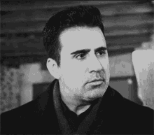 a black and white photo of a man with a beard wearing a coat and scarf .