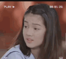 a young girl in a school uniform is looking at the camera with a play button in the corner .