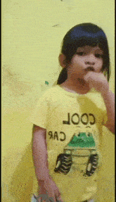a little girl is wearing a yellow shirt that says cool on it
