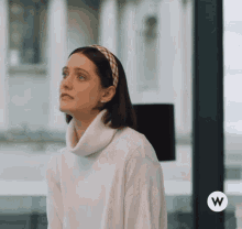 a woman wearing a headband and a white sweater with the letter w on the bottom right