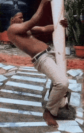 a shirtless man leans against a pole while holding a large piece of paper