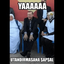 a man in a suit is sitting in a blue chair next to a group of women .