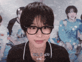a young man wearing glasses is smiling in front of a group of people