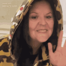 a woman wearing a camo hoodie is smiling and waving