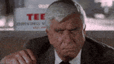 a man in a suit stands in front of a sign that says tee driving school