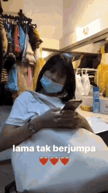 a woman wearing a face mask is looking at her phone in a dressing room .