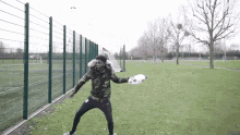 a man in a camouflage jacket is throwing a soccer ball in a field