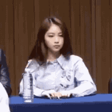 a young woman is sitting at a table with a bottle of water .