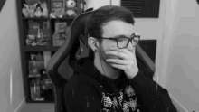 a man wearing glasses and headphones is sitting in a chair and covering his mouth with his hand .