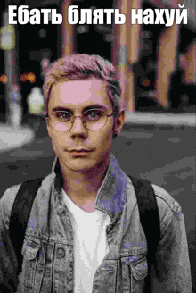 a young man with pink hair and glasses is wearing a denim jacket and a white shirt .