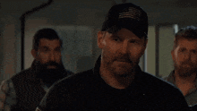 a group of men are standing next to each other in a room . one of the men is wearing a hat .