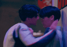 two young men are hugging and kissing each other in front of a wall .