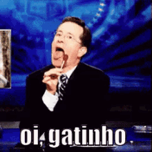 a man in a suit and tie is holding a lollipop in his mouth and says oi gatinho on the bottom