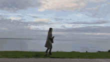 a woman in a coat is walking along the shore of a lake