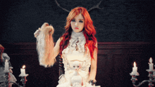 a woman with red hair is holding a doll and a wig