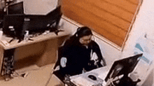 a woman is sitting at a desk in front of a computer monitor .