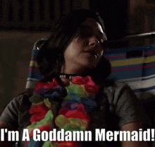 a woman sitting in a chair with a lei around her neck and the words " i 'm a goddamn mermaid " below her