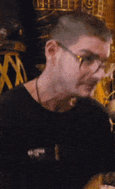 a man wearing glasses and a black shirt is standing in a dark room .