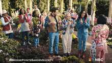 a group of people standing in a garden with a nbc logo on the bottom right