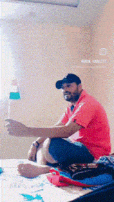 a man in a red shirt and black hat is sitting on a bed holding a small flag