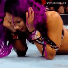 a female wrestler with purple hair is kneeling on the ground .