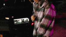 a man in a plaid jacket stands in front of a car